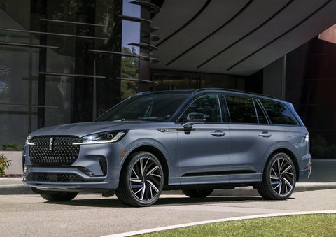 A gray 2025 Lincoln Aviator® SUV is parked outside a modern building showcasing the driver’s side of the vehicle. | Joe Cooper Lincoln of Edmond in Oklahoma City OK