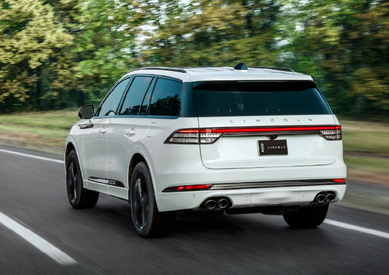 A white 2026 Lincoln Aviator® SUV is being driven away down a road lined with colorful trees. | Joe Cooper Lincoln of Edmond in Oklahoma City OK