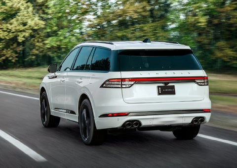 A white 2026 Lincoln Aviator® SUV is being driven away down a road lined with colorful trees. | Joe Cooper Lincoln of Edmond in Oklahoma City OK