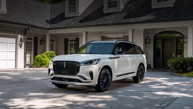 A white 2026 Lincoln Aviator® SUV is parked in the driveway of a luxury home. | Joe Cooper Lincoln of Edmond in Oklahoma City OK